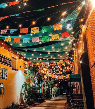 bishop arts district at night an alley way with Papel Picado flapping in the wind interspersed with string lights