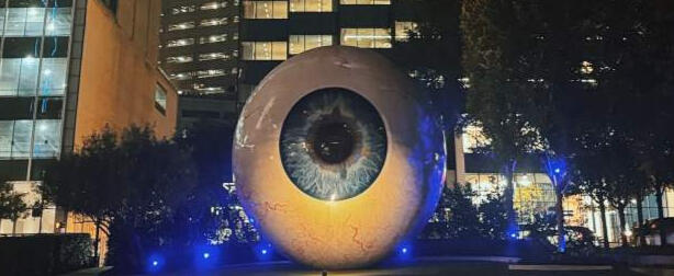 A photo from one of our true crime walking tours showing the big red court house at dusk the clock tower is lit in a warm glow a crowd of people gather to listen to our guide tell his story